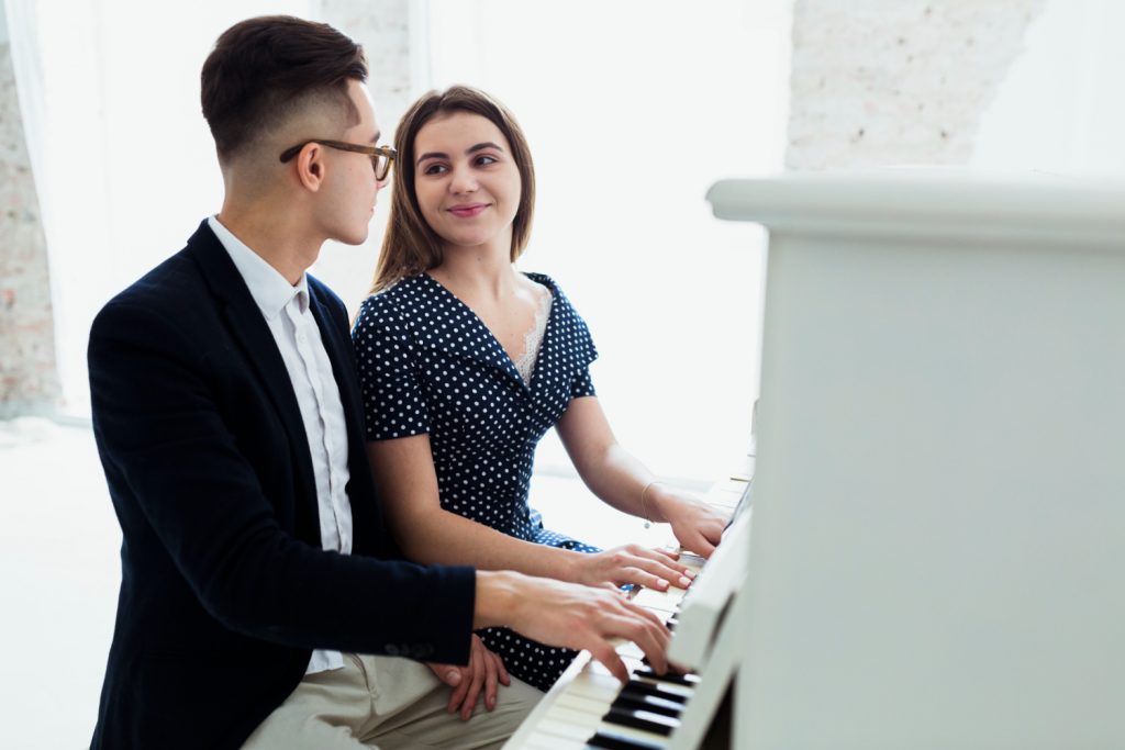 casal a olharem-se amorosamente e a tocarem piano